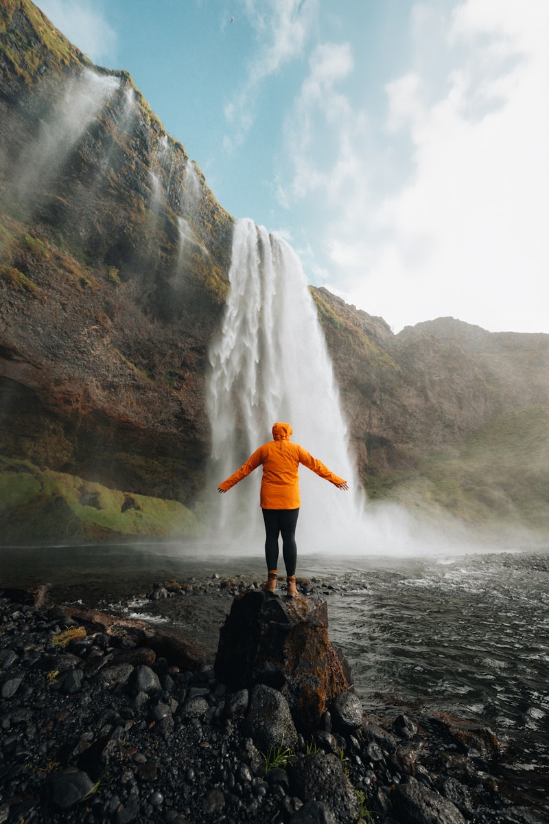 Photo by Karsten Winegeart A person standing on a rock in front of a waterfall